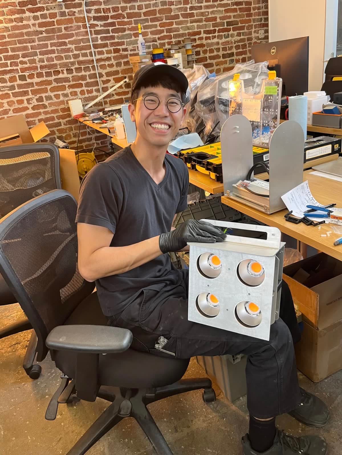 Harrison Lin in the San Francisco workshop, smiling with a freshly assembled Rhythm light engine on his lap